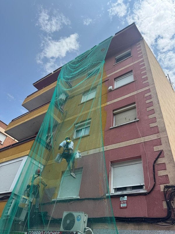 Dos operarios descolgados con cuerdas pintando la fachada de una comunidad
