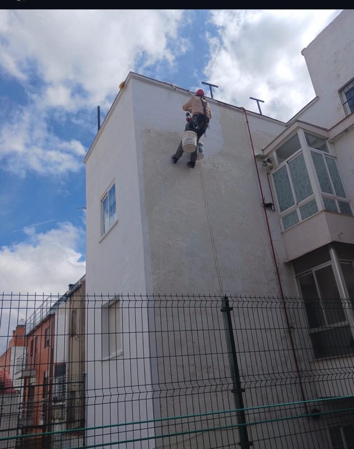 Operario descolgado con cuerdas saneando la fachada, sin andamio